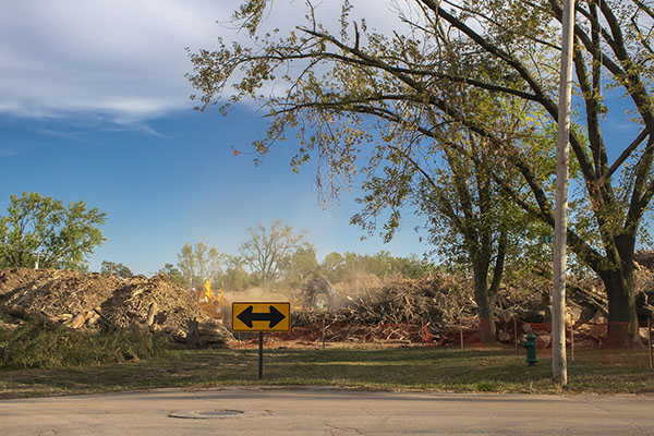 A tractor lifts wood debris in Time Check, while wood chippers process it, producing a dust cloud. In front of it, there is a sign indicating you must turn right or left; the road ends